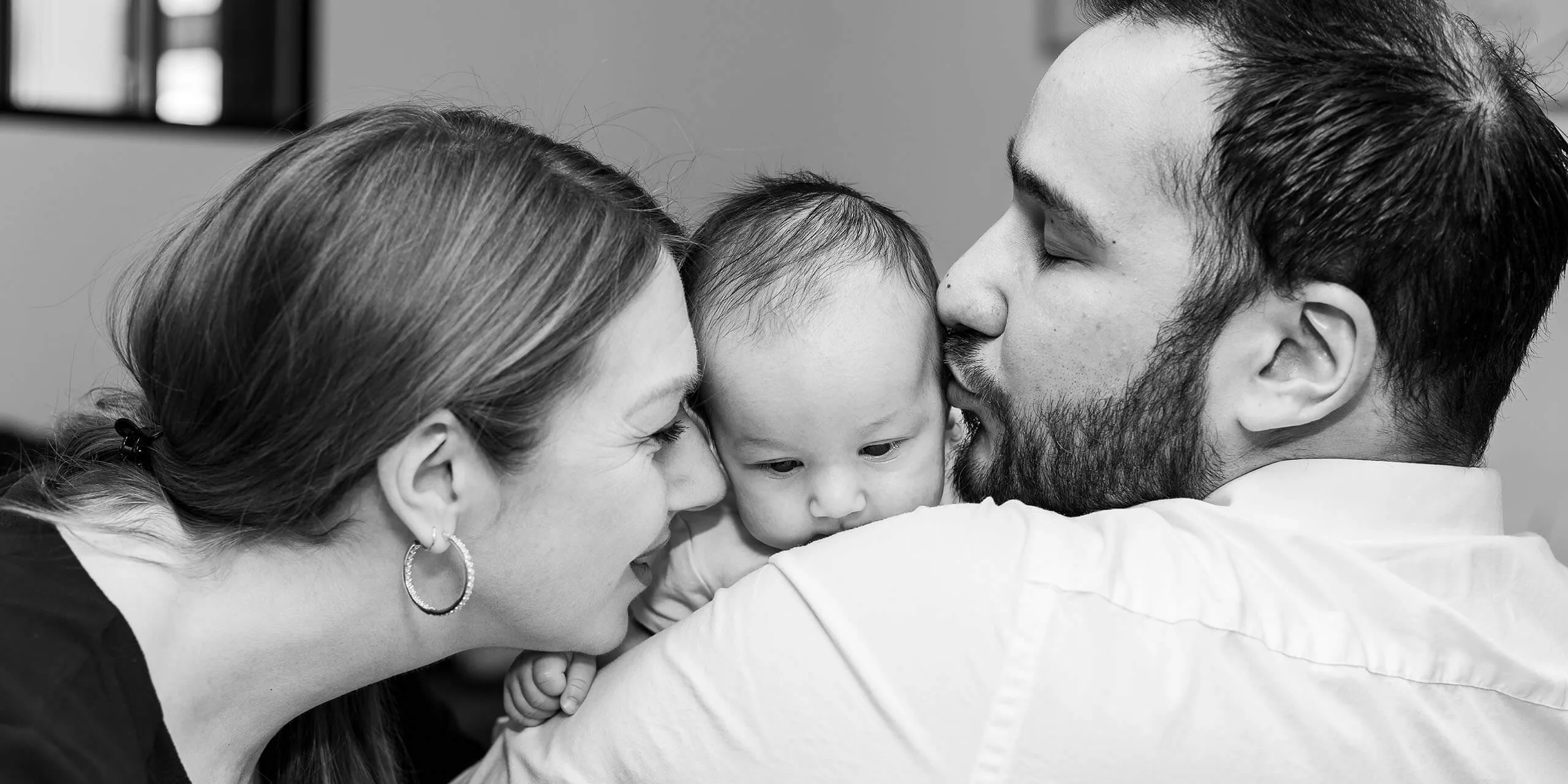 Parents embrassant tendrement leur nouveau-né lors d'une séance photo à domicile à Strasbourg - Photographe naissance Bas-Rhin