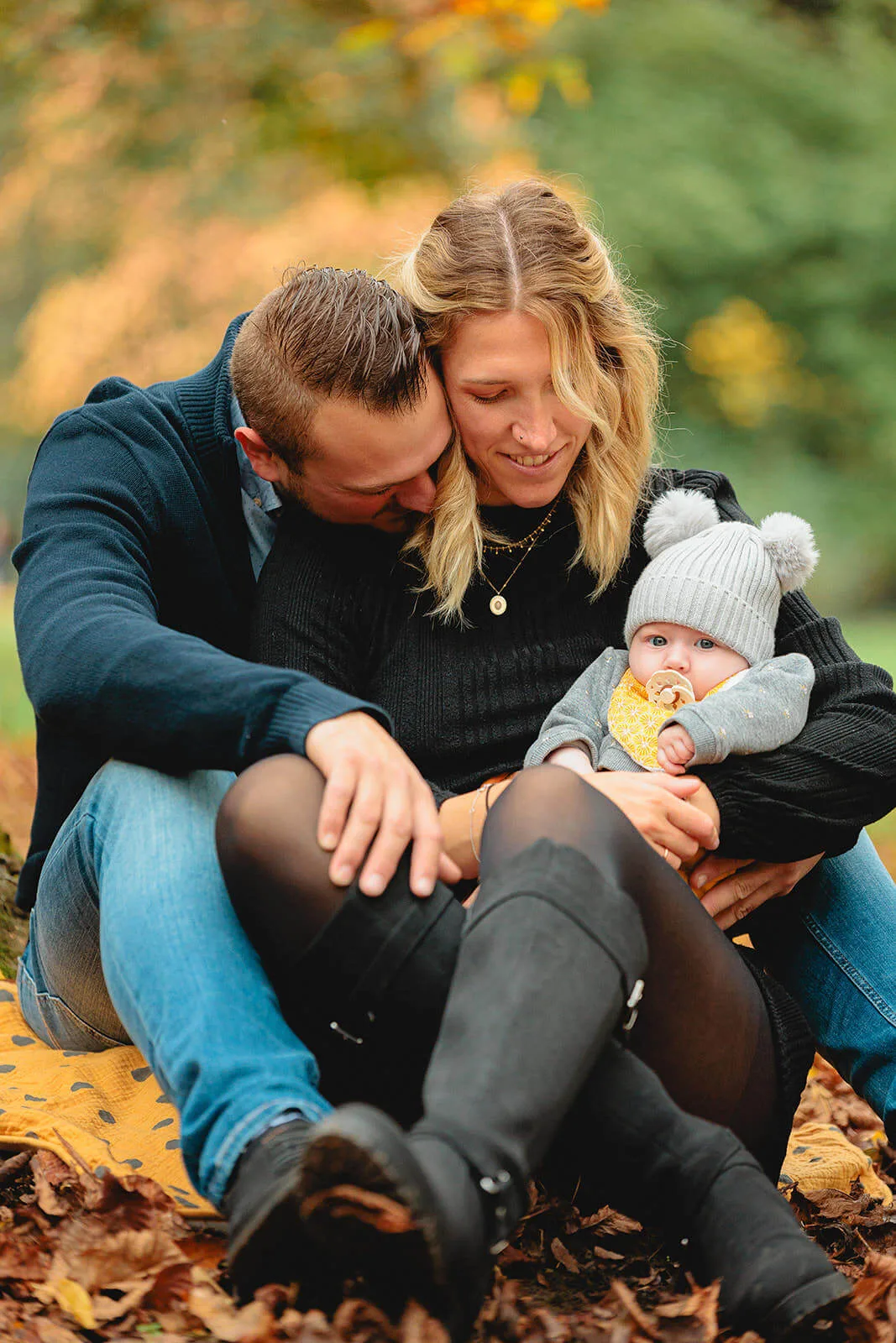 Parents assis enlacés sur des feuilles d'automne, tenant leur bébé dans les bras au parc de l'Orangerie