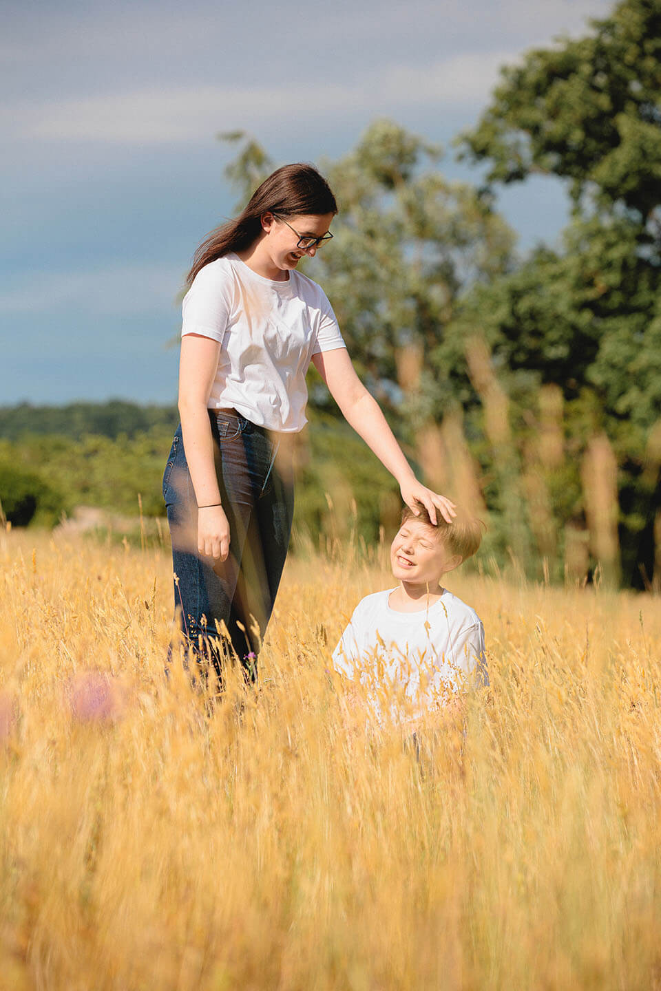 Séance photo famille — complicité entre frère et sœur dans les herbes hautes en été