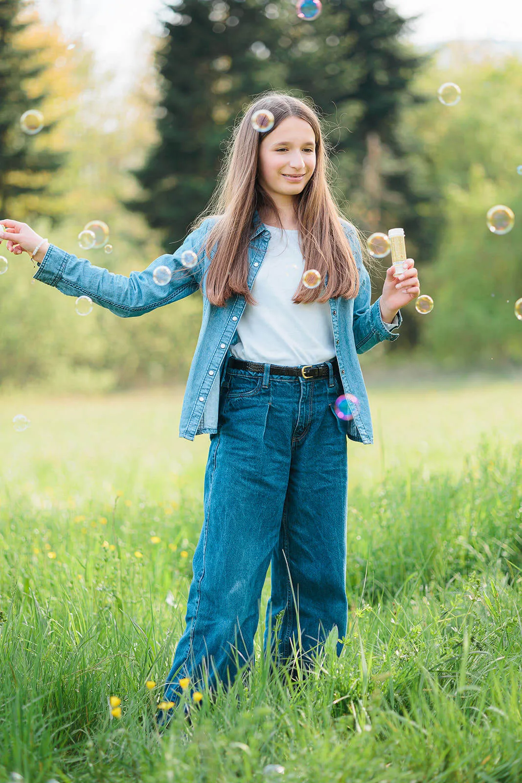 Jeune fille en tenue en jean entourée de bulles de savon dans une prairie au parc de la Léonardsau