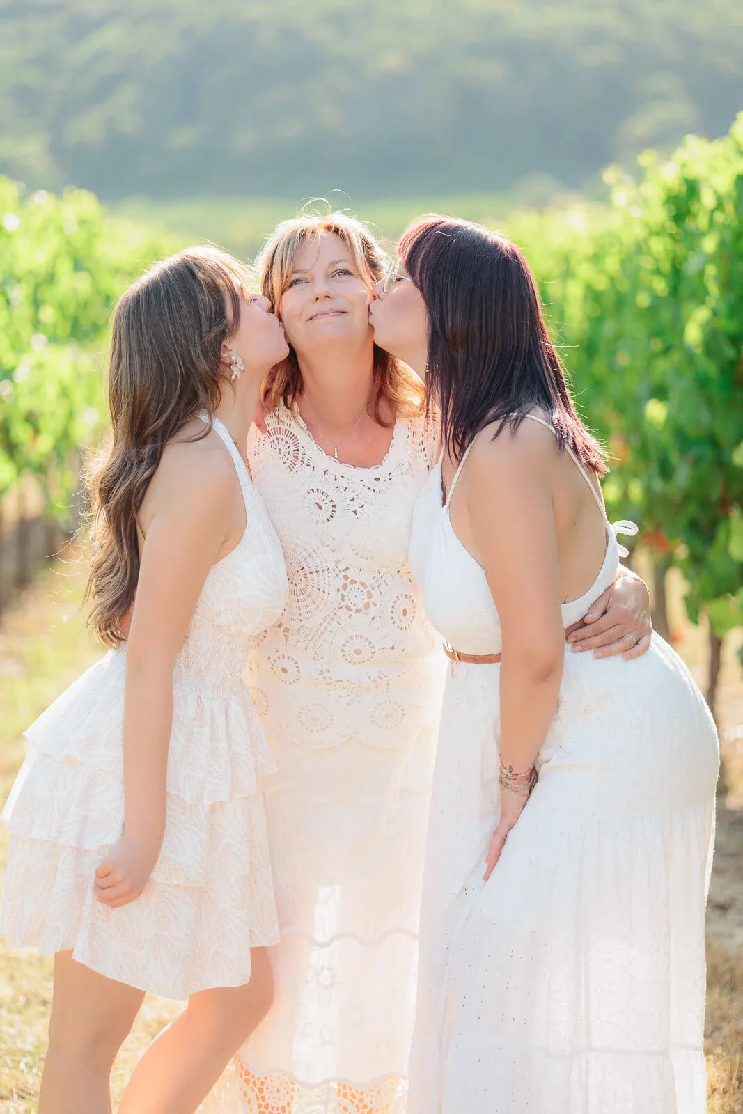 Séance photo famille dans les vignes près d'Obernai, mère entourée de ses deux filles en robes blanches