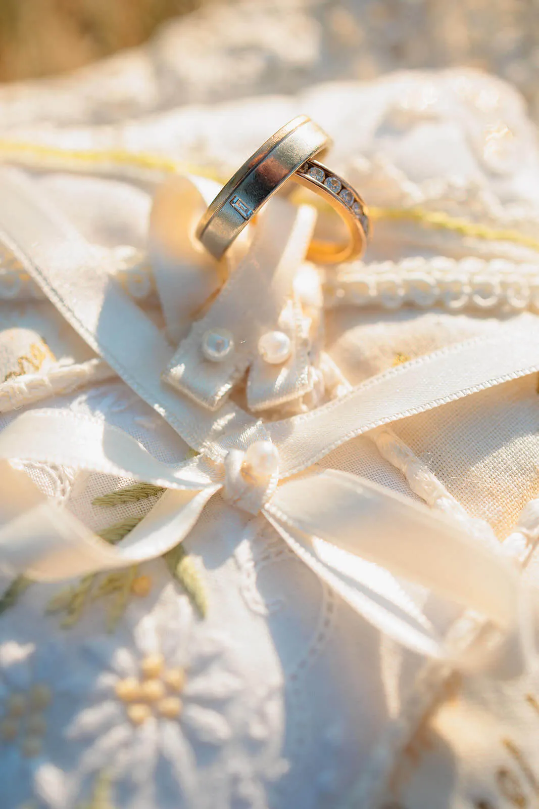 Gros plan sur deux alliances posées sur un coussin brodé de dentelle et de perles