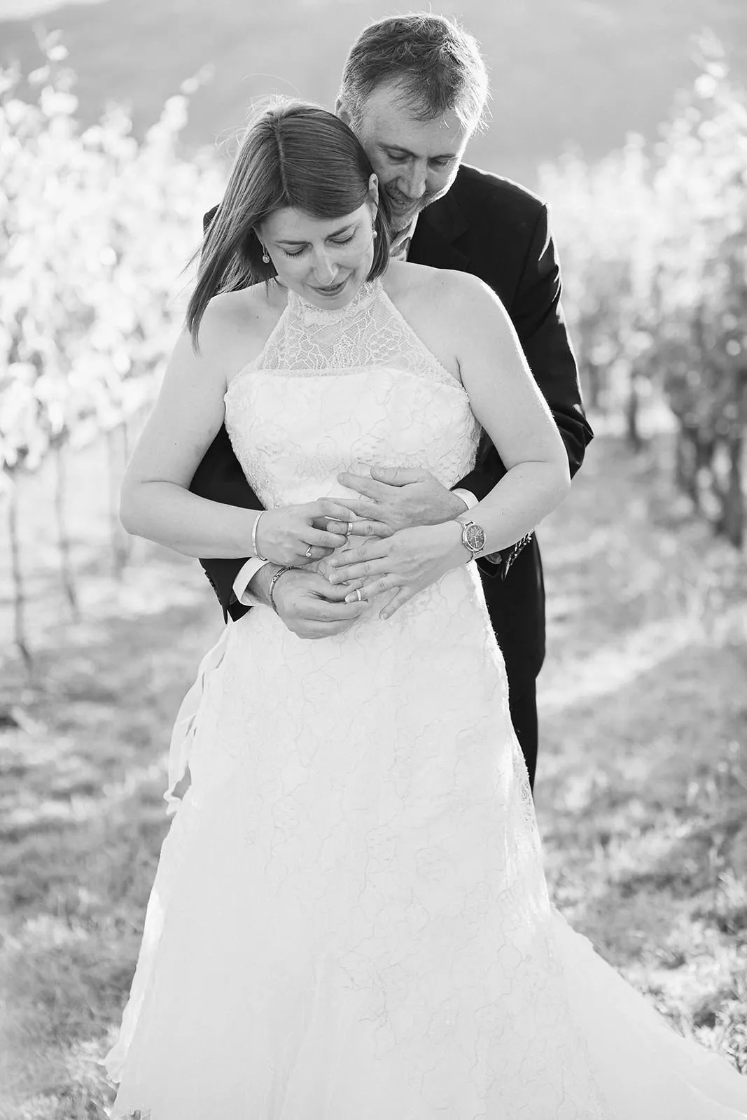 Portrait noir et blanc d'un couple enlacé, mains jointes sur leurs alliances, au milieu d'un vignoble