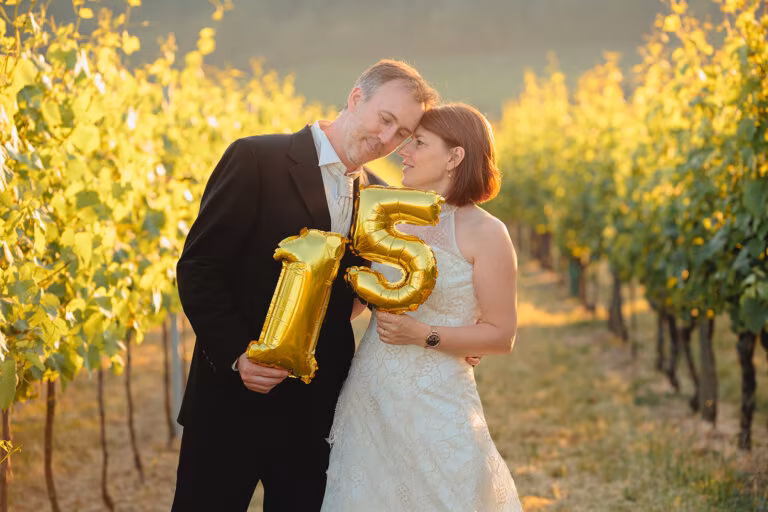 Couple célébrant 15 ans de mariage avec des ballons dorés, lumière dorée dans un vignoble d'Alsace