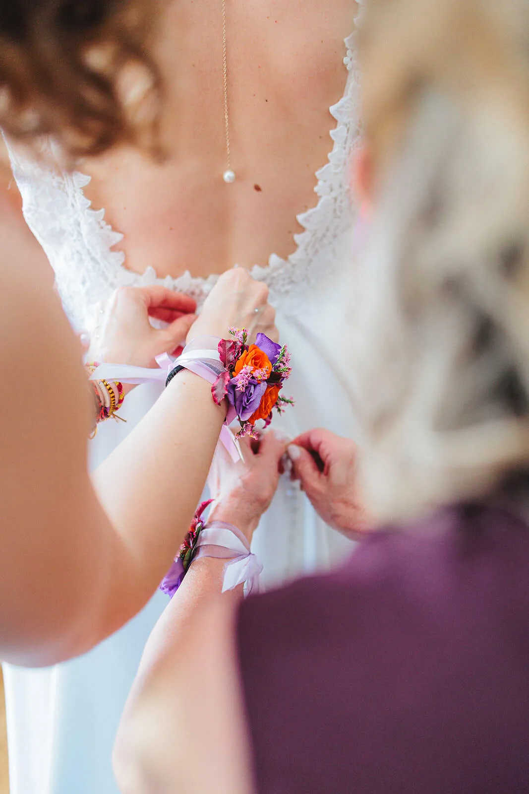Bracelet floral attaché au poignet de la témoin qui aide à fermer la robe de la mariée avant la cérémonie