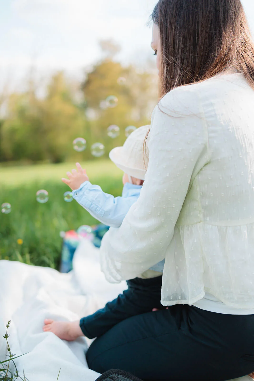 Bébé émerveillé par des bulles de savon dans les bras de sa maman, moment de douceur dans le parc de la Léonardsau.
