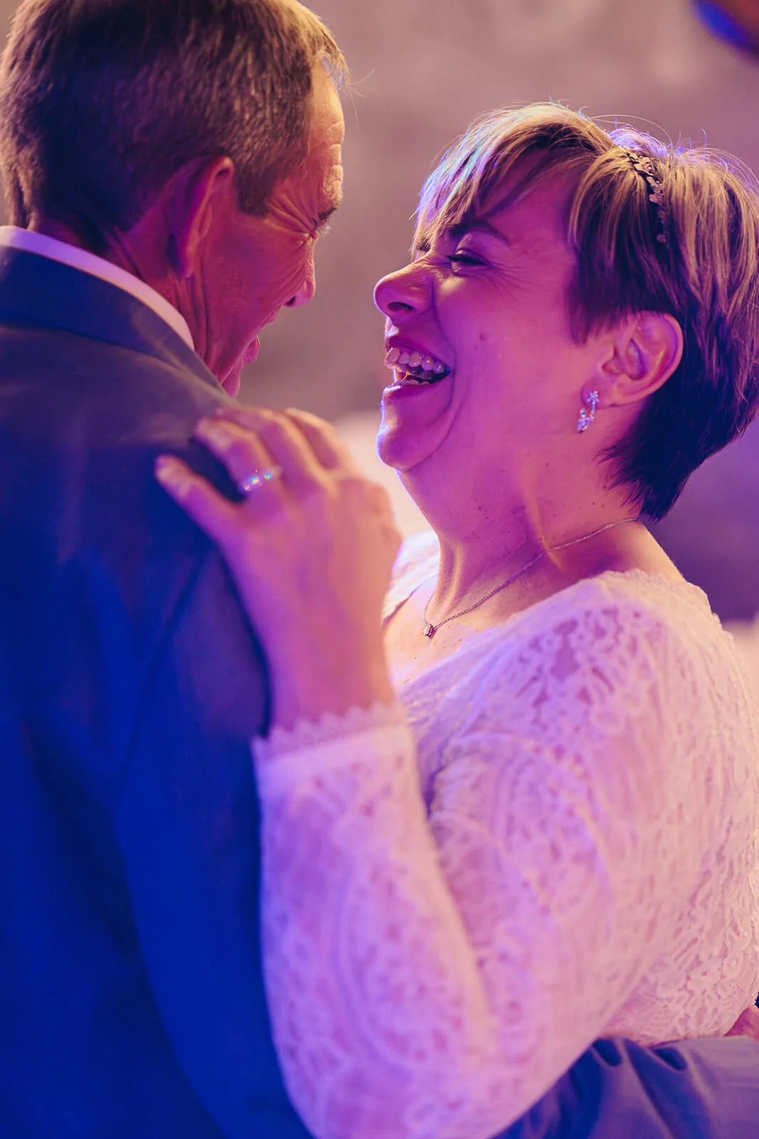 Mariée riant aux éclats en dansant avec le marié, ambiance lumineuse colorée