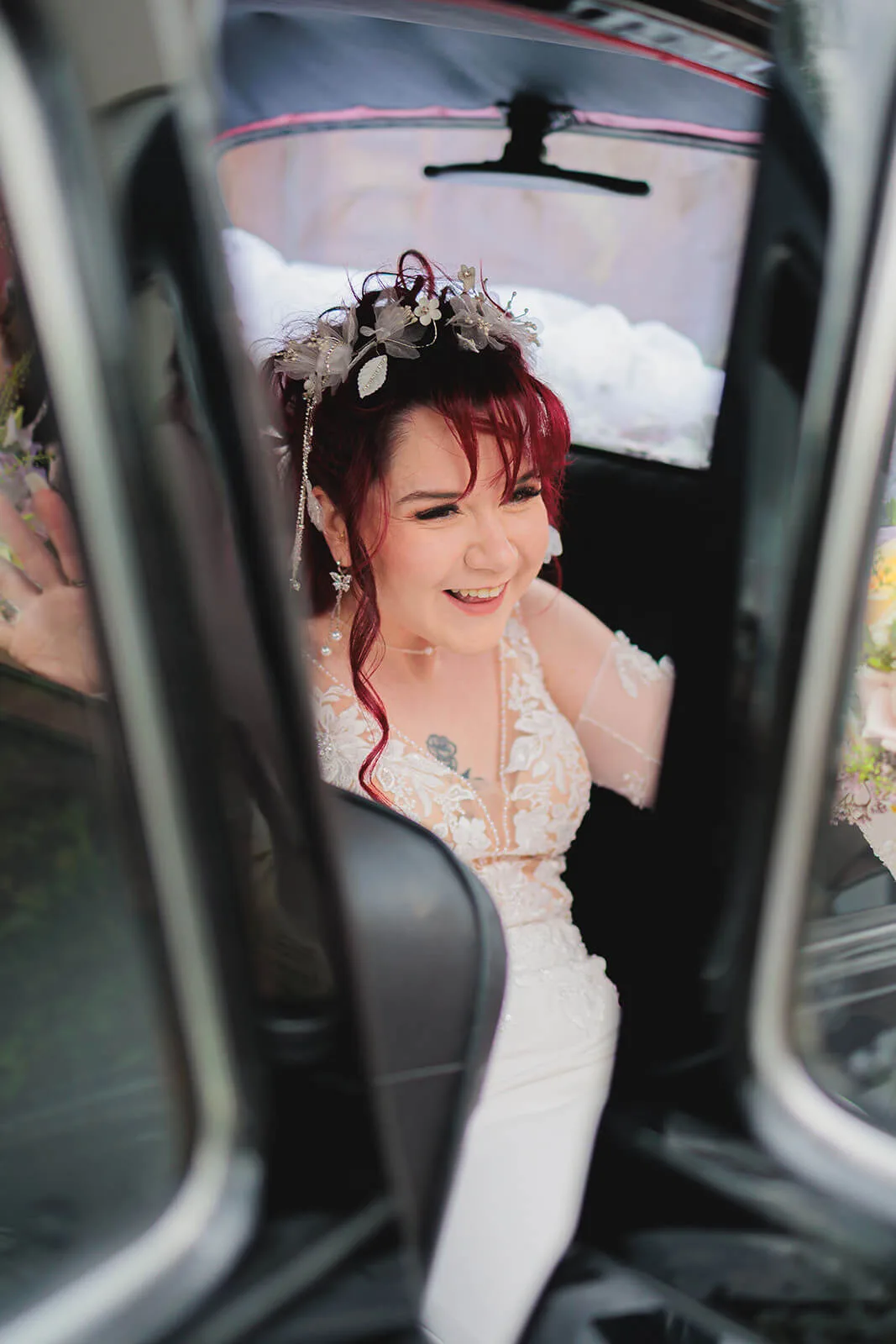 Mariée souriante capturée à la sortie de la voiture, coiffure fleurie
