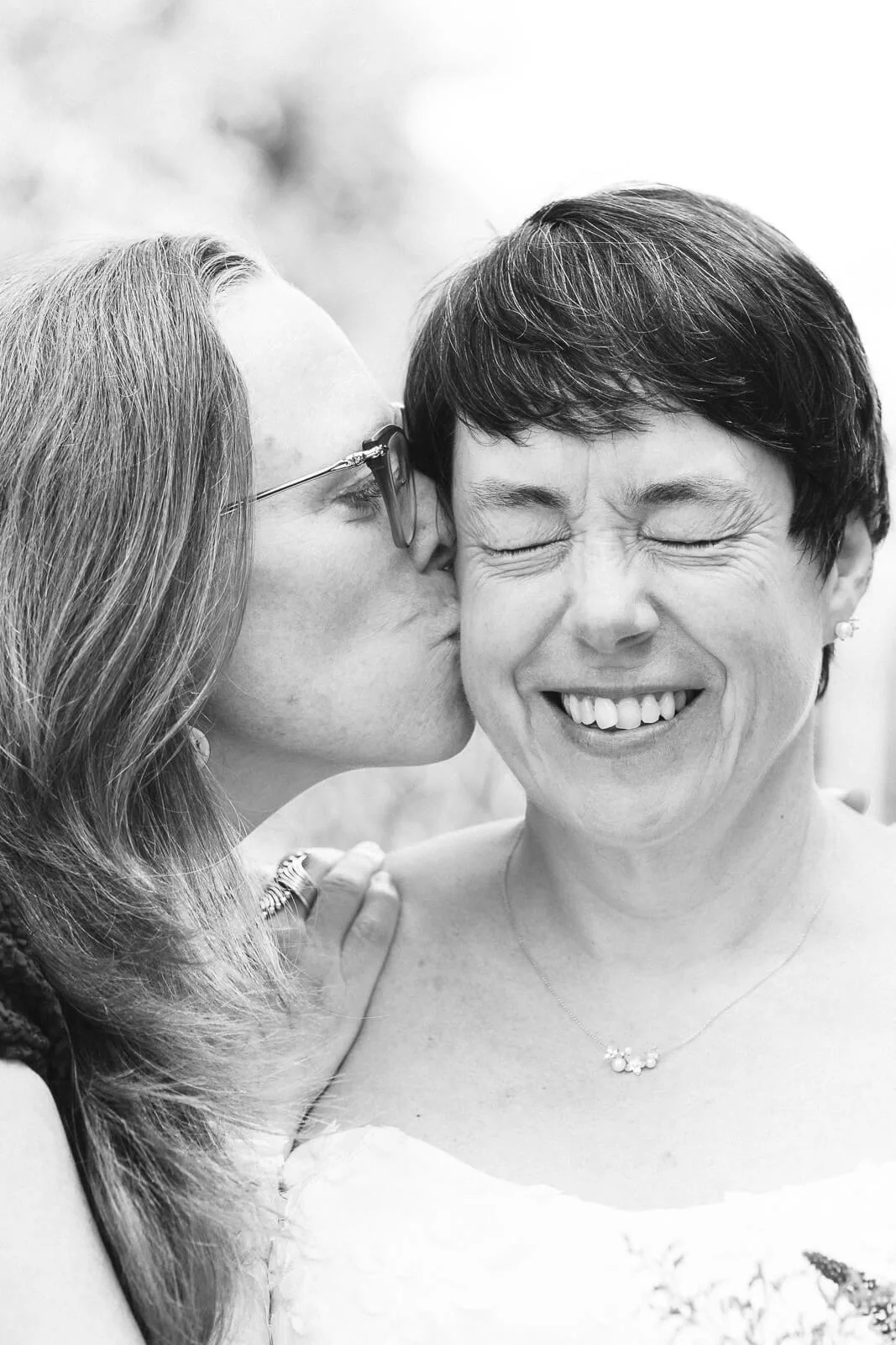 Bise tendre et complice entre la mariée et sa meilleure amie, photo noir et blanc