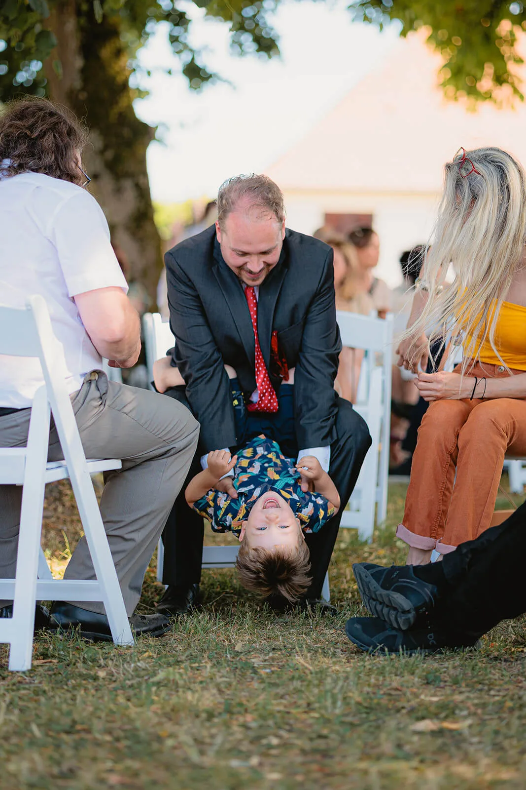 Invité tenant un enfant à l'envers pendant le vin d'honneur en extérieur